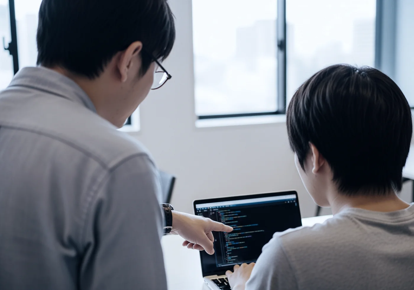 メンターがラップトップの画面を指してコードを教えている学習風景